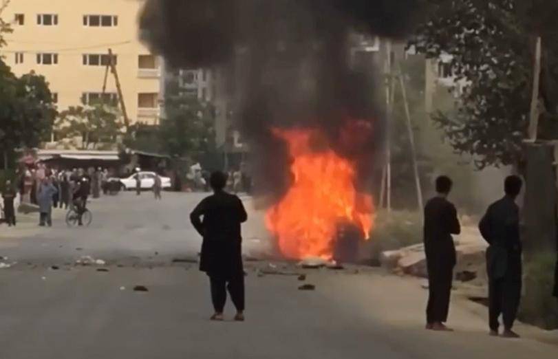 People gather around remnants of flames from cars where rockets towards Kabul's international airport were fired from but were intercepted by a missile defense system in Kabul