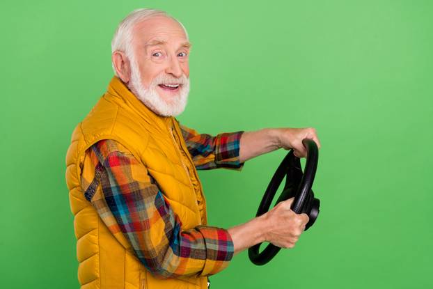 Photo of excited charming mature man dressed yellow waistcoat smiling riding auto isolated green color background