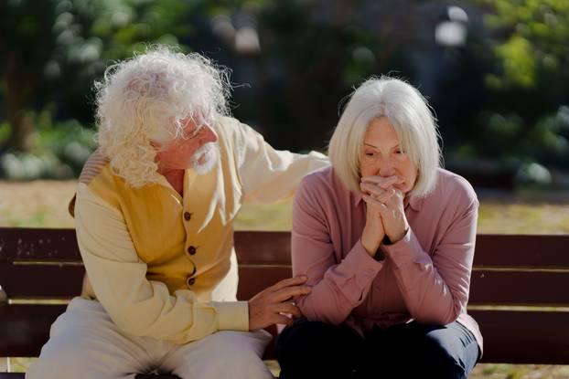 Senior sad couple sitting on bench outdoors