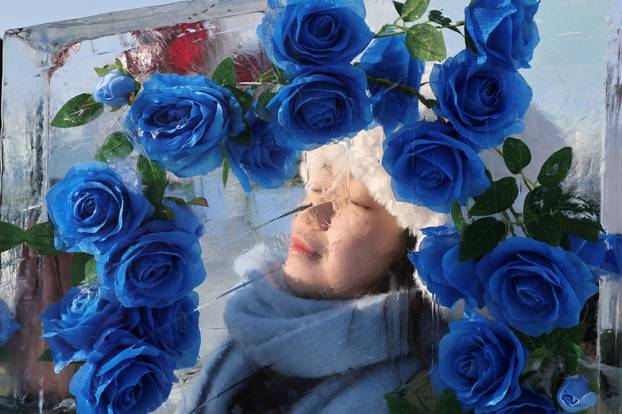 A person poses behind an ice pillar at the annual Ice and Snow Festival in Harbin