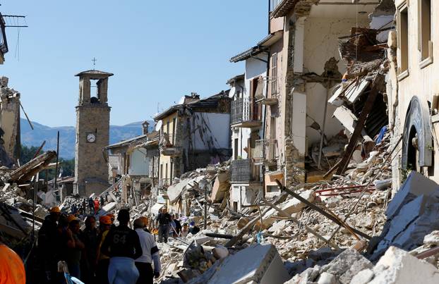 FILE PHOTO: People stand next collapsed buildings following an earthquake in Amatrice