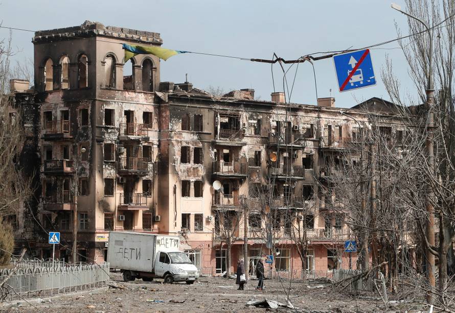 Local residents walk along a street next to a damaged building in Mariupol