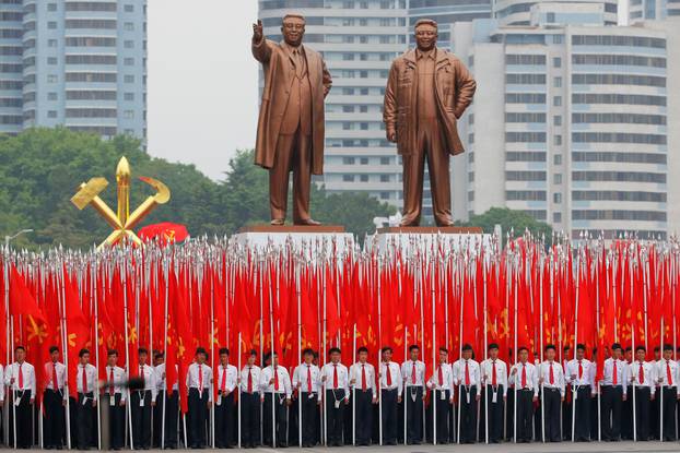 Students carrying party flags stand under statues of former North Korean leaders Kim Il Sung and Kim Jong Il at the beginning of a mass rally and parade in Pyongyang