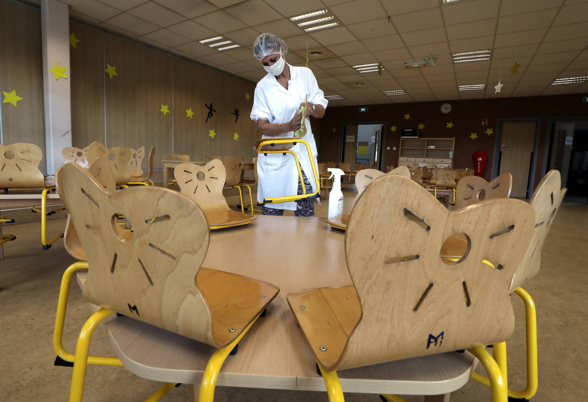 A municipal employee, wearing a protective face mask, cleans chairs in the canteen at a primary school in Le Cannet