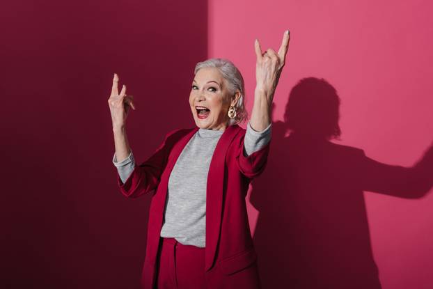Fashionable old lady making rock and roll sign and shouting indoors