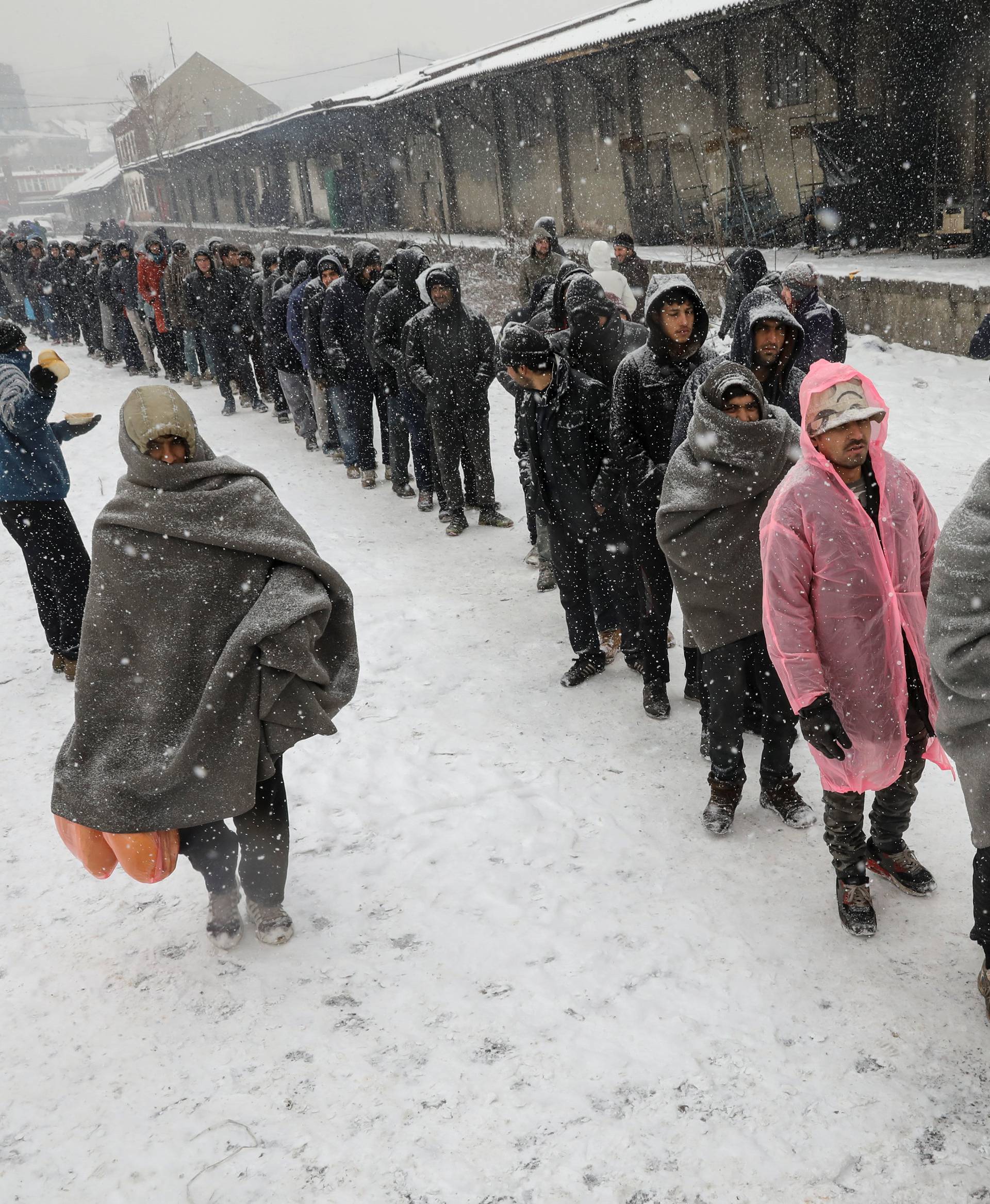 Migrants stand in line to receive free food outside a derelict customs warehouse in Belgrade