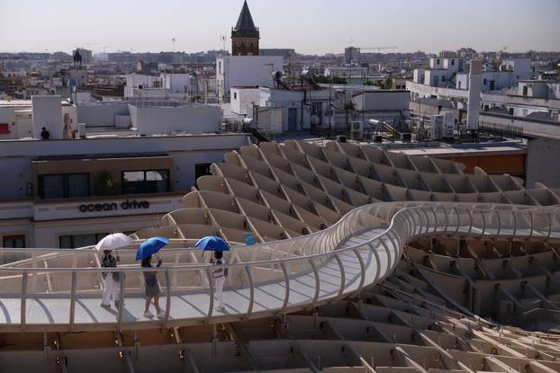 Tourists walk with umbrellas on Las Setas during a heatwave in Seville