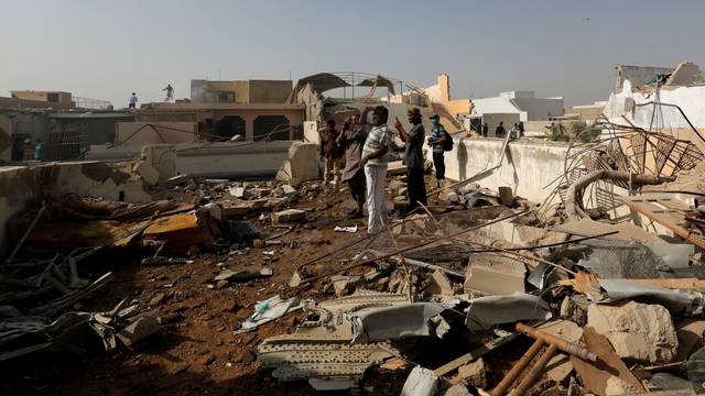 People stand on a roof of a house amidst debris of a passenger plane, crashed in a residential area near an airport in Karachi