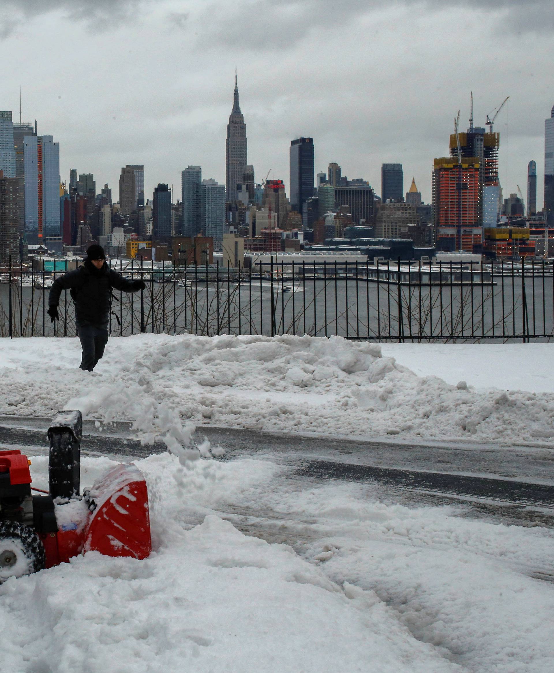 A resident clears the street of snow in Weehawken, New Jersey, as the Empire State Building and Middle Manhattan are seen after a snowstorm in New York