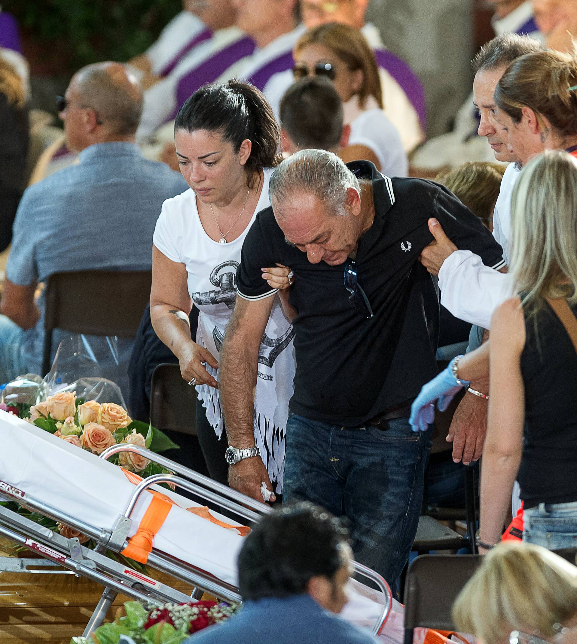 A man is helped by Red Cross members during a funeral service for victims of the earthquake inside a gym in Ascoli Piceno, Italy