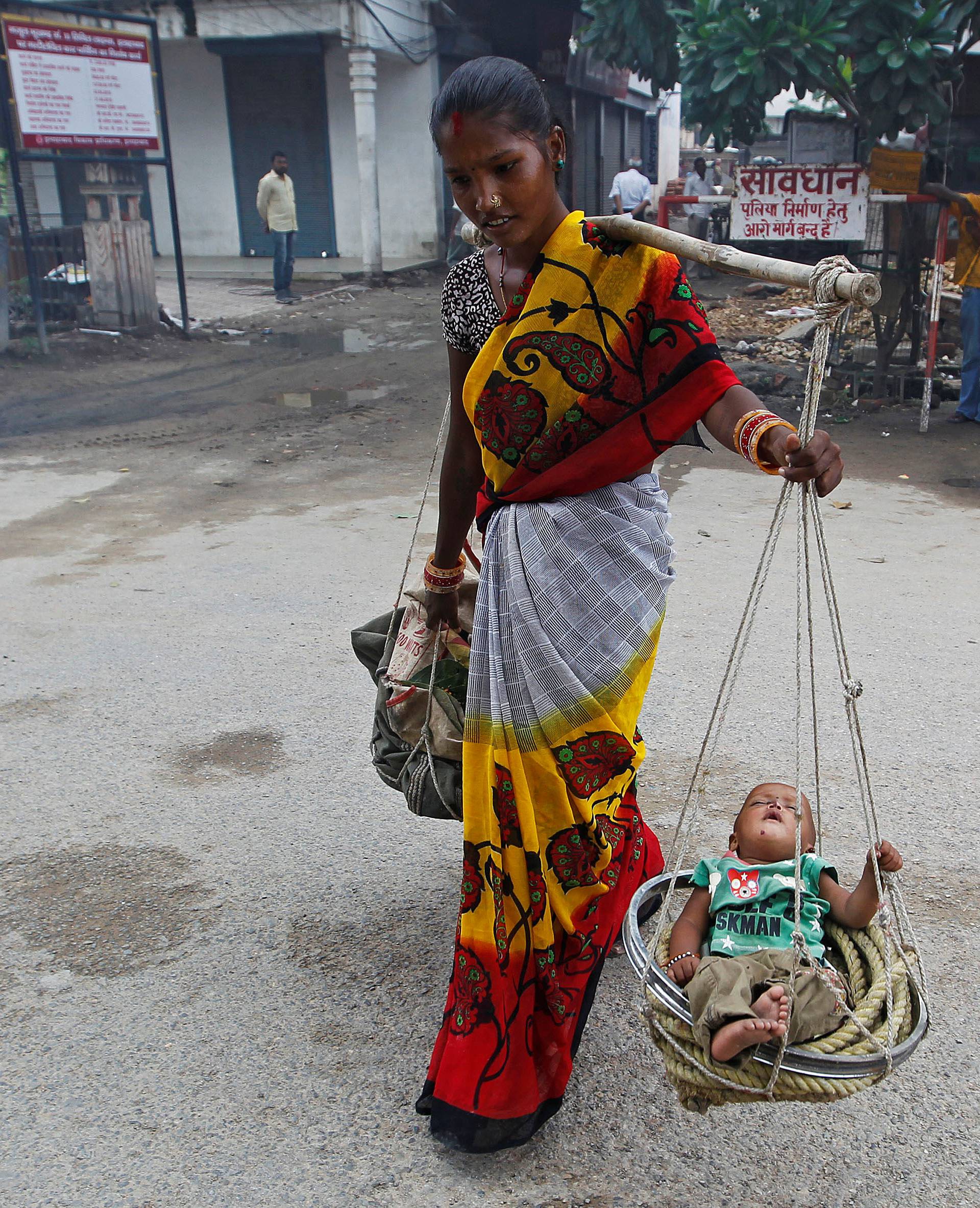 A woman carries her child in a basket as she walks on a road in Allahabad
