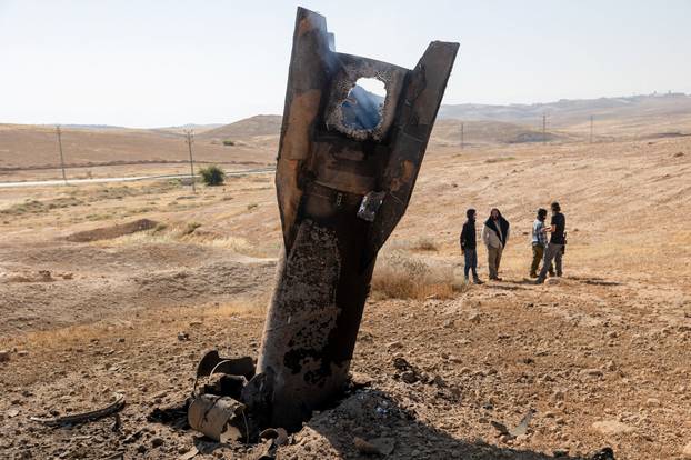 Israeli settlers stand next to part of a missile protruding from the ground, following strikes from Iran, in the central Israeli-occupied West Bank