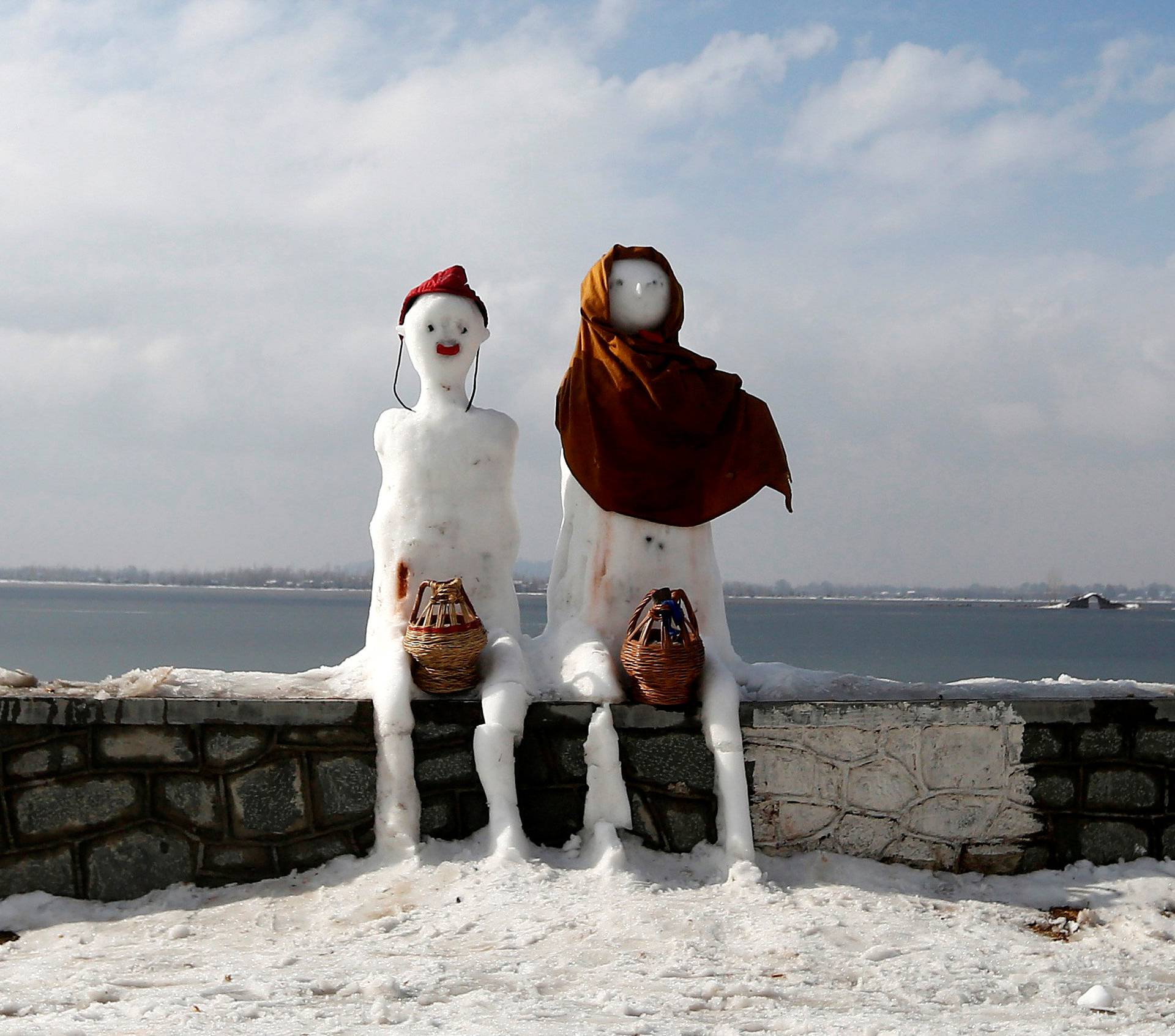 A snow man and a snow woman with "Kangris", traditional fire pots, are installed on the banks of Dal Lake in Srinagar