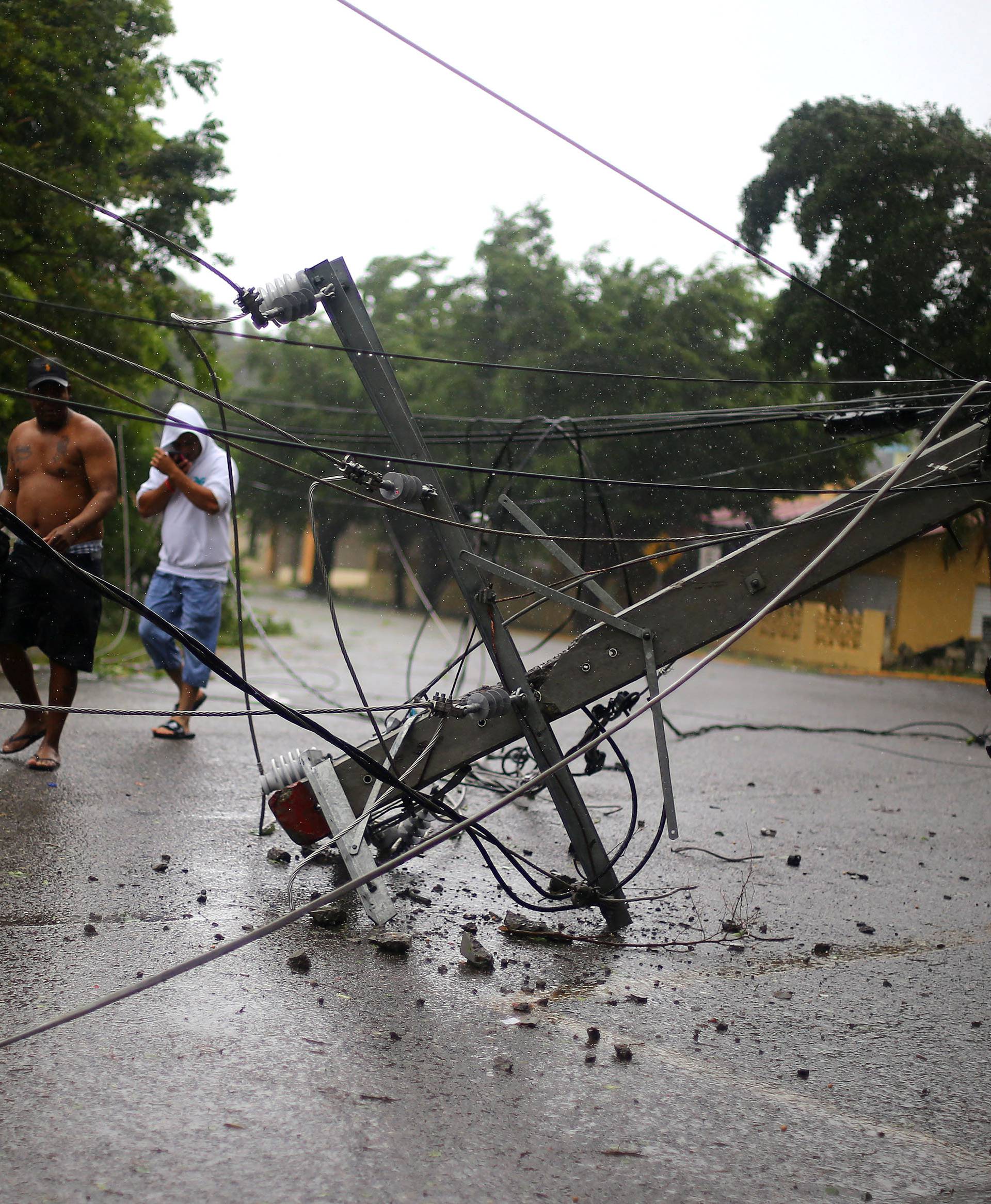 Locals walk past a fallen power pole as Hurricane Irma moves off the northern coast of the Dominican Republic, in Puerto Plata