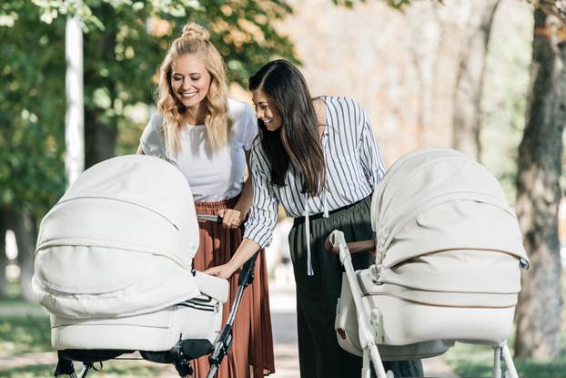 smiling mothers looking in baby stroller in park