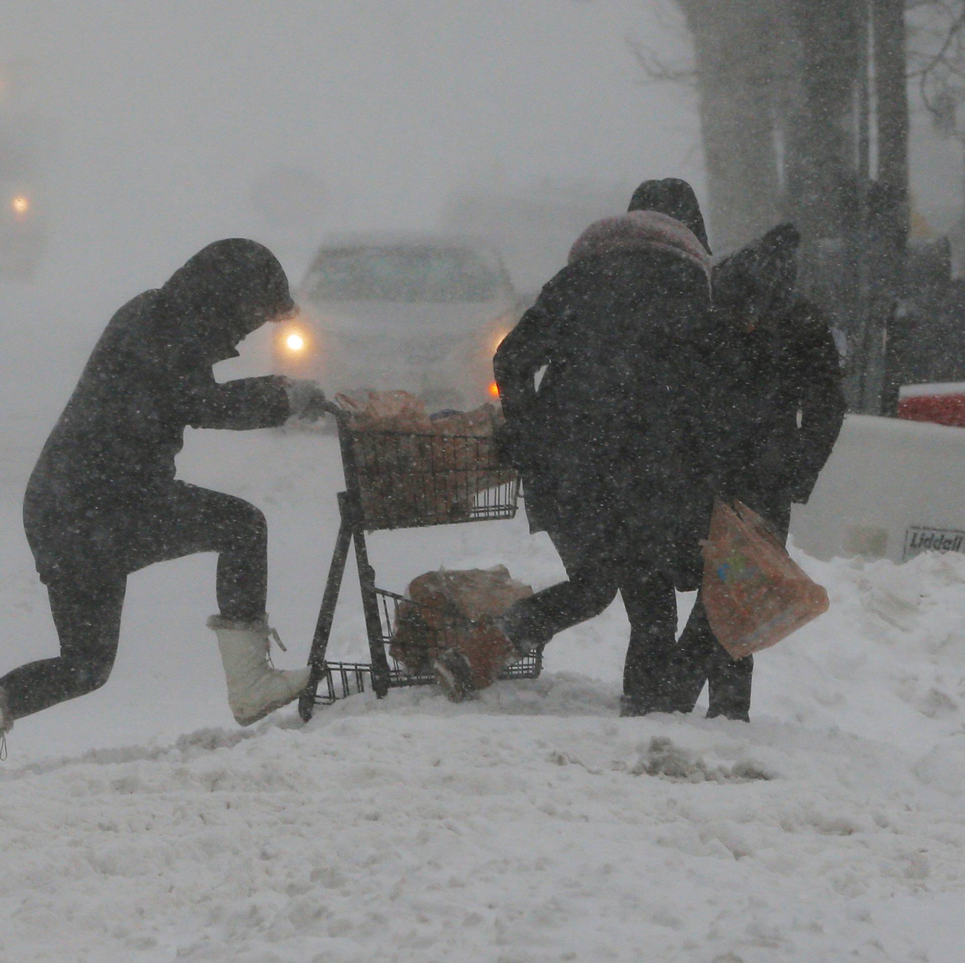 People push a shopping cart carrying firewood over a snow bank during Storm Grayson in Boston
