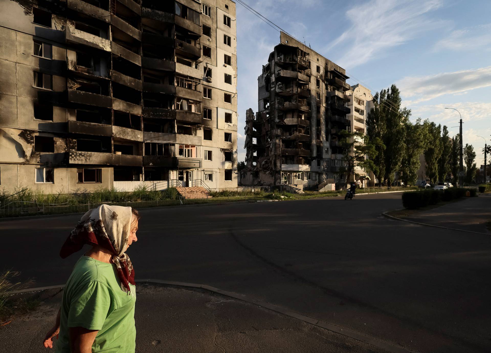 A woman walks down a street in front of destroyed buildings in Borodianka