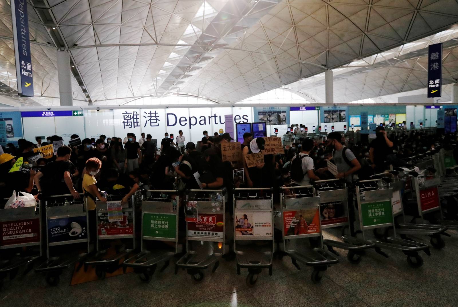 Anti-government protesters stand at a barricade made of trolleys during a demonstration at Hong Kong Airport