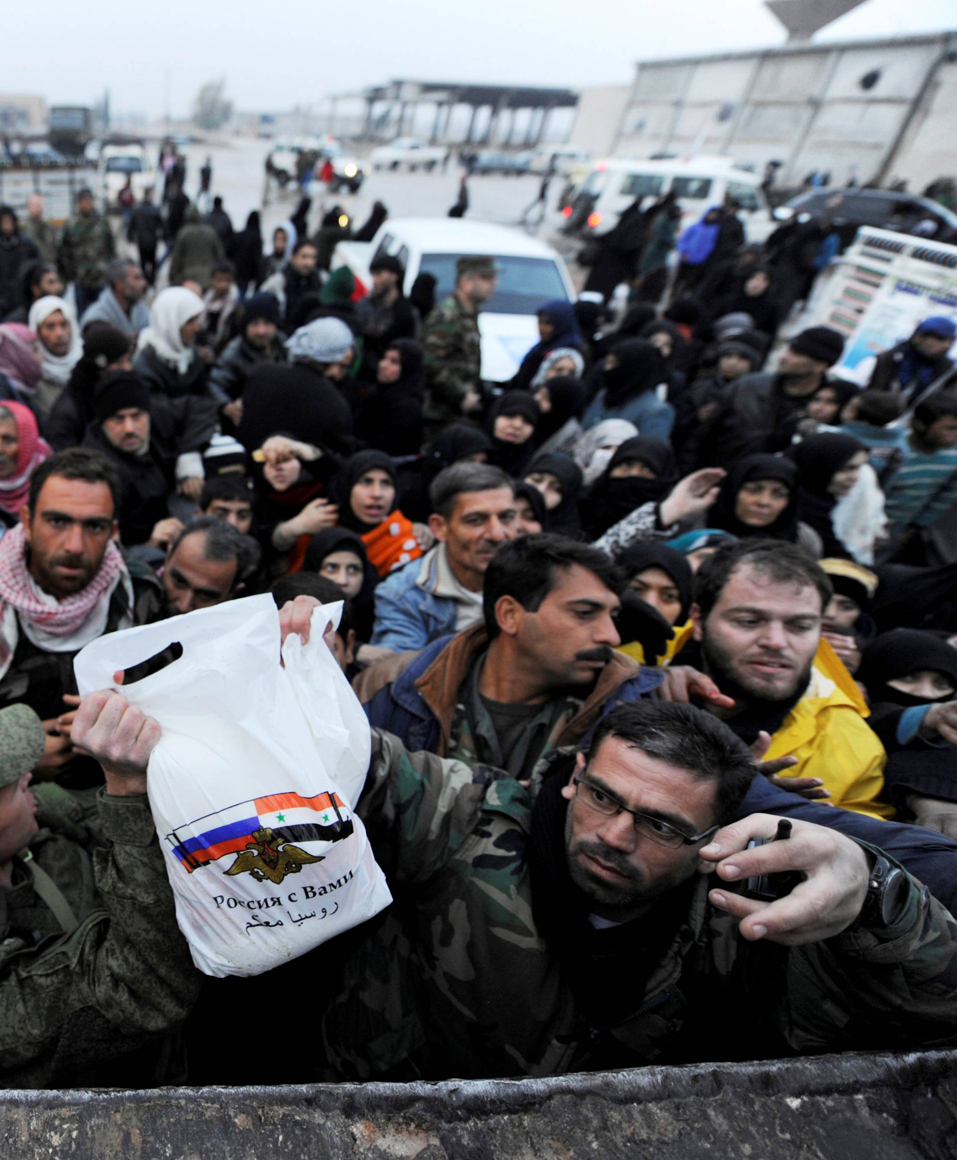 Syrians evacuated from eastern Aleppo, among with a Russian soldier and a Syrian government soldier carry a Russian food aid bag in government controlled Jibreen area in Aleppo