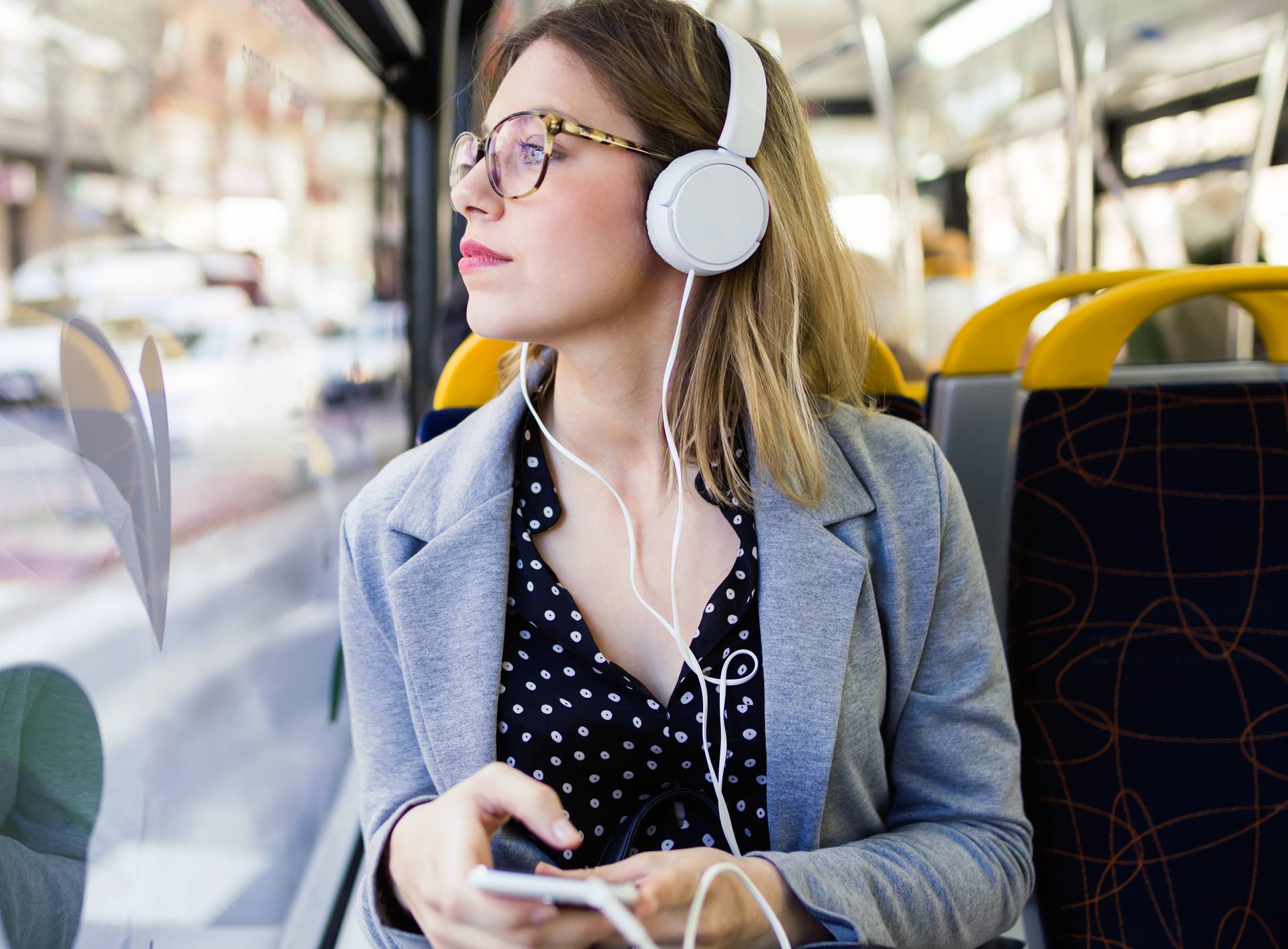 Pretty young woman listening to music with mobile phone at the bus.