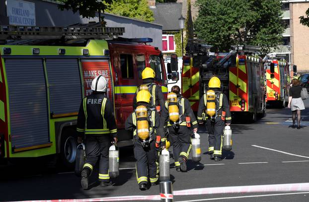Firefighters carry gas cylinders near a tower block severly damaged by a serious fire, in north Kensington, West London