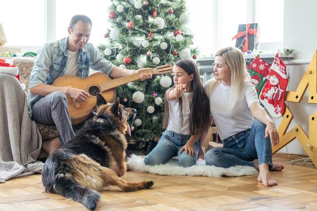 smiling family and daughter with dog sitting near christmas tree with gifts