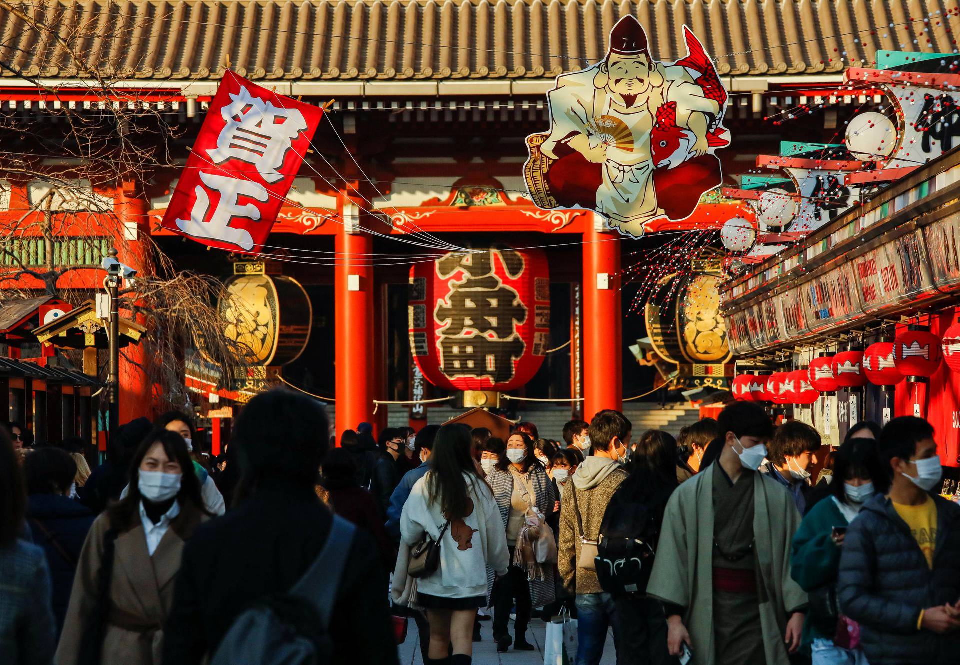 Visitors wearing protective face masks walk under decorations for the New Year at Nakamise street leading to Senso-ji temple at Asakusa district in Tokyo