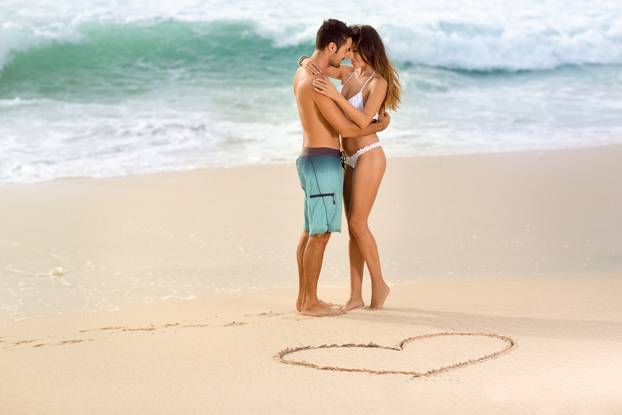 Love couple on beach with drawing heart in sand