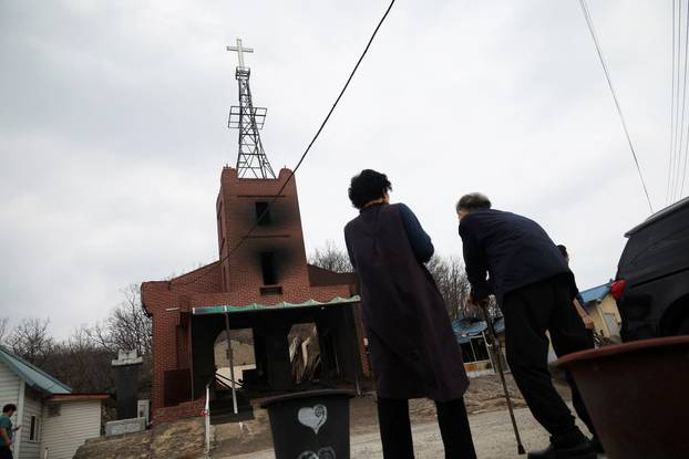 People stand near a burnt church after a wildfire devastated the area, in Uiseong