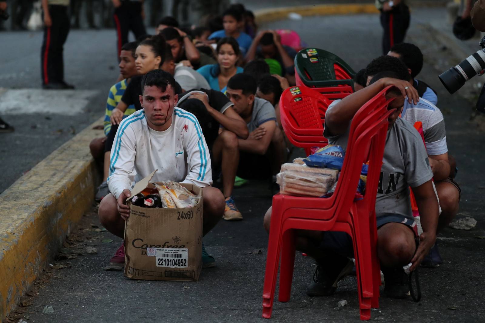 Men sit on a street as they are detained by security forces after looting during an ongoing blackout in Caracas