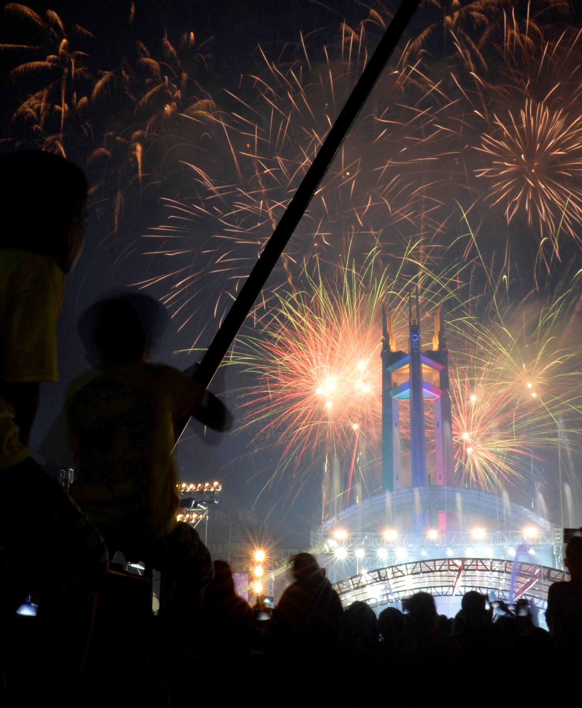 Revellers watch as fireworks explode over the Quezon Memorial Circle during New Year's celebrations in Quezon City, Metro Manila