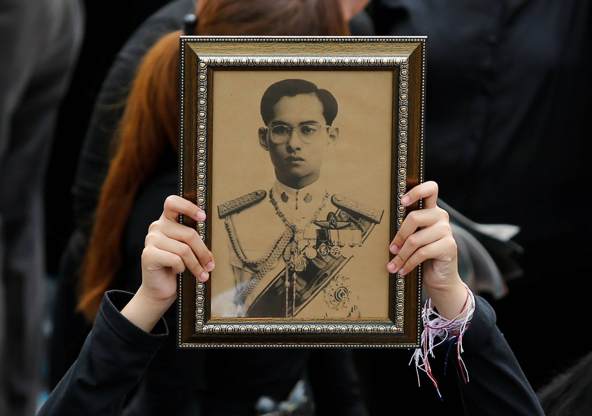 A woman holds an image of King Bhumibol Adulyadej as mourners gather outside of the Grand Palace to sing for a recording of the royal anthem in honour of their king, in Bangkok