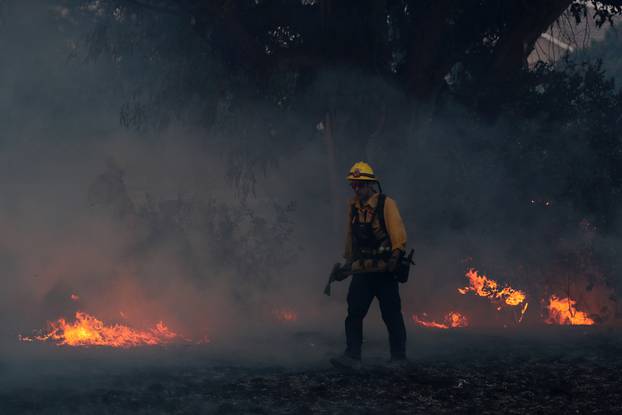 A firefighter works to put out hot spots on a fast moving wind driven wildfire in Orange, California