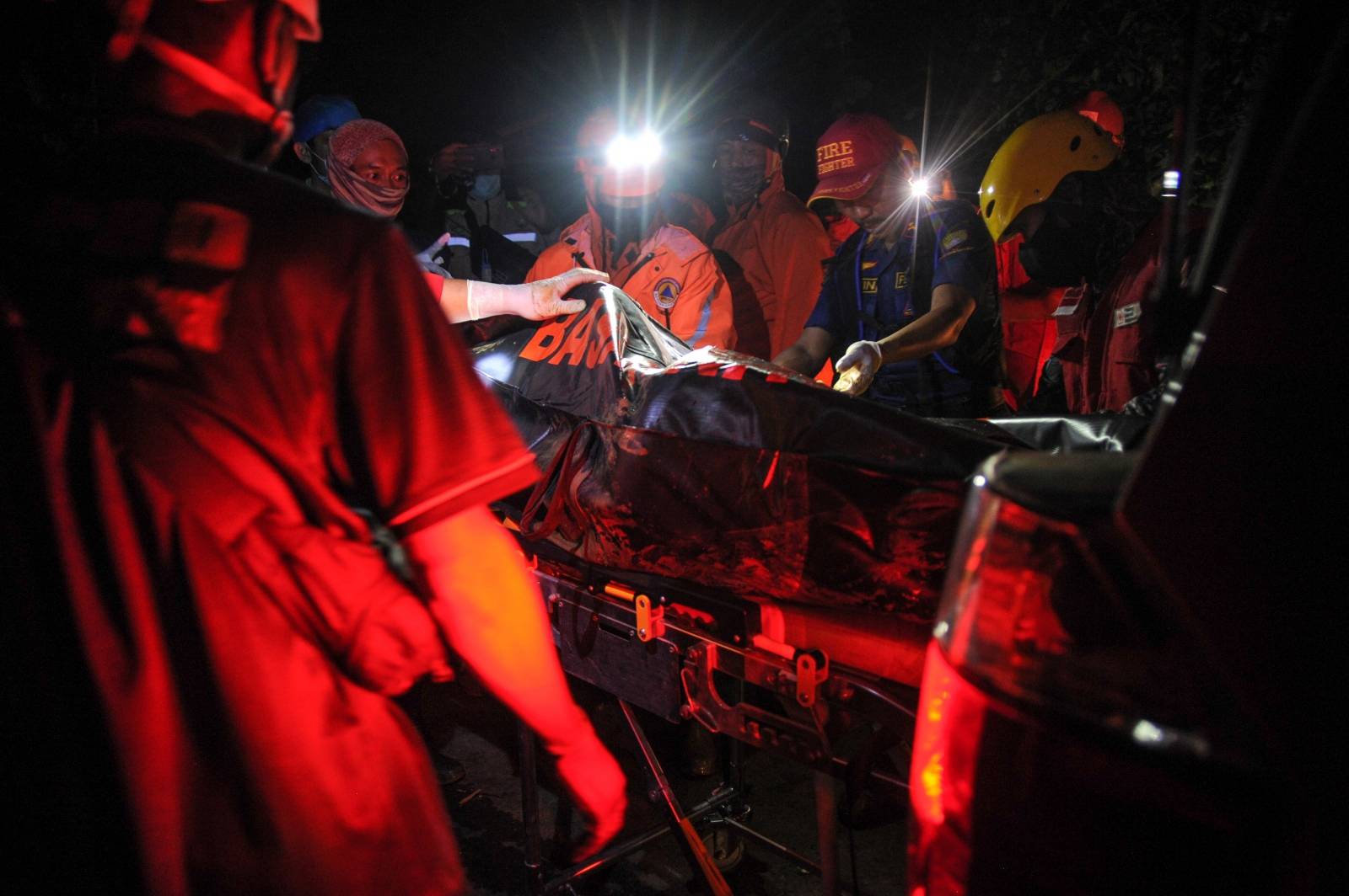 Rescue personnel transport a body bag containing a victim of a bus that fell into a ravine in Sumedang, Indonesia
