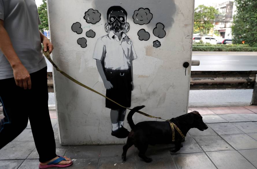 FILE PHOTO: A woman walks a dog in front of a graffiti of Thai artist Headache Stencil which makes a reference to the air quality in Bangkok