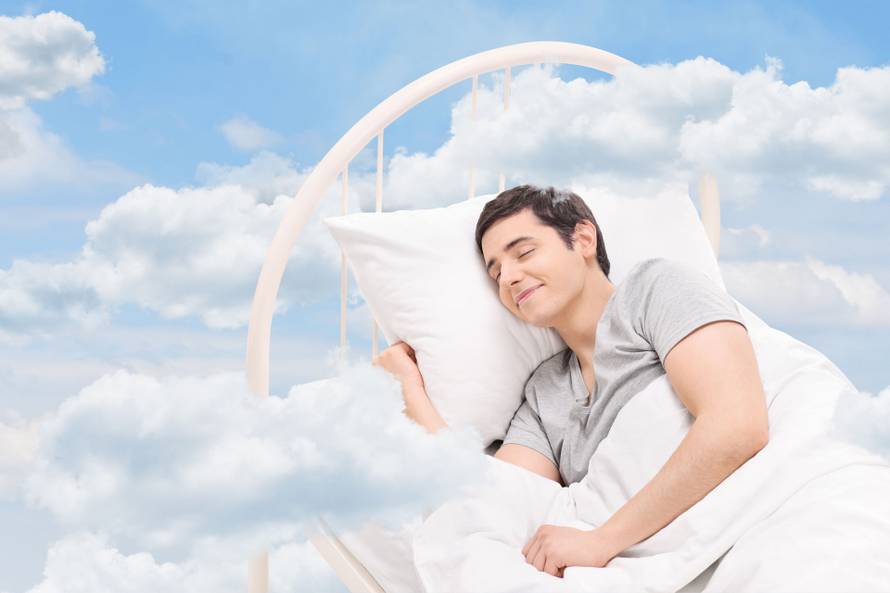 Joyful man sleeping on a bed in the clouds