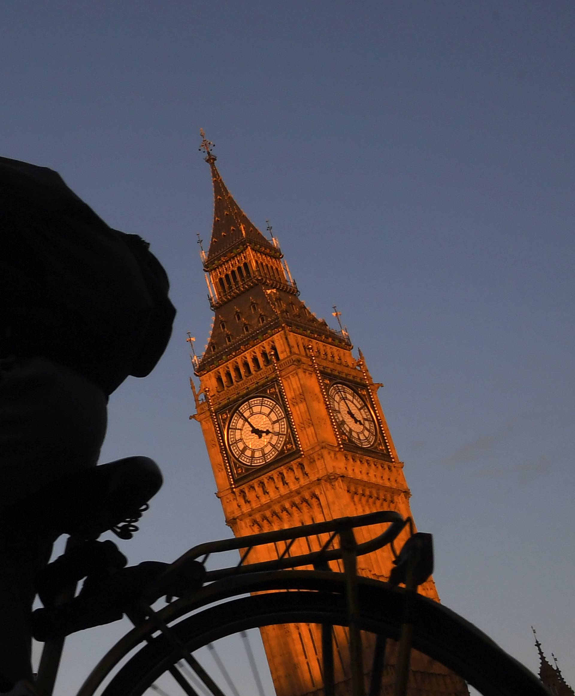 A man cycles past past Big Ben and the Houses of Parliament in late afternoon sunlight in London