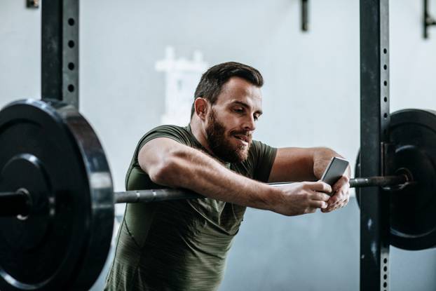 Caucasian,Sportsman,Typing,On,His,Cell,Phone,At,Gym.