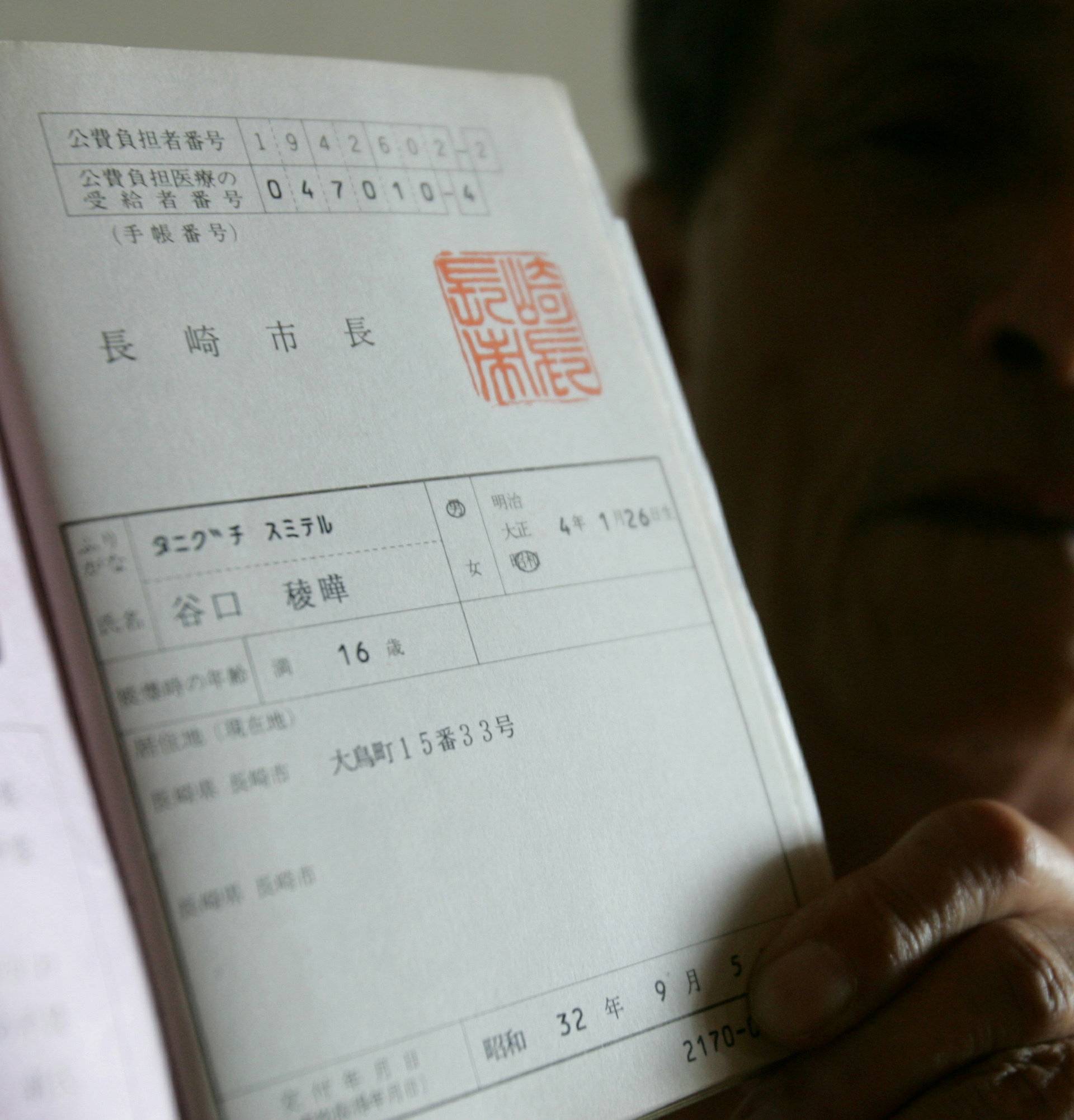 FILE PHOTO: Atomic bomb victim Sumiteru Taniguchi shows his bomb-survivor's health card at his home in Nagasaki