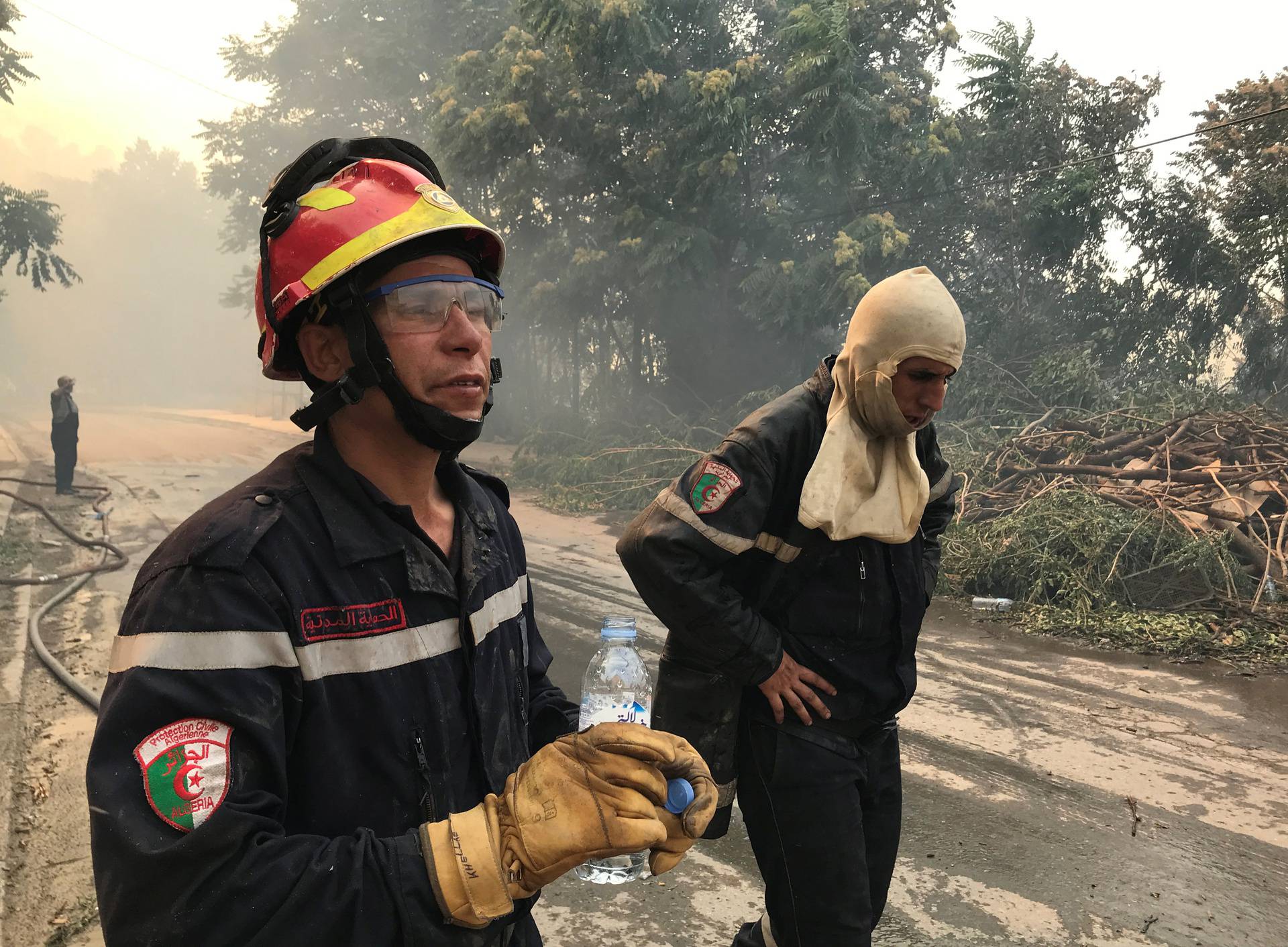 Firefighters stand along a road during a forest fire in Ain al-Hammam village