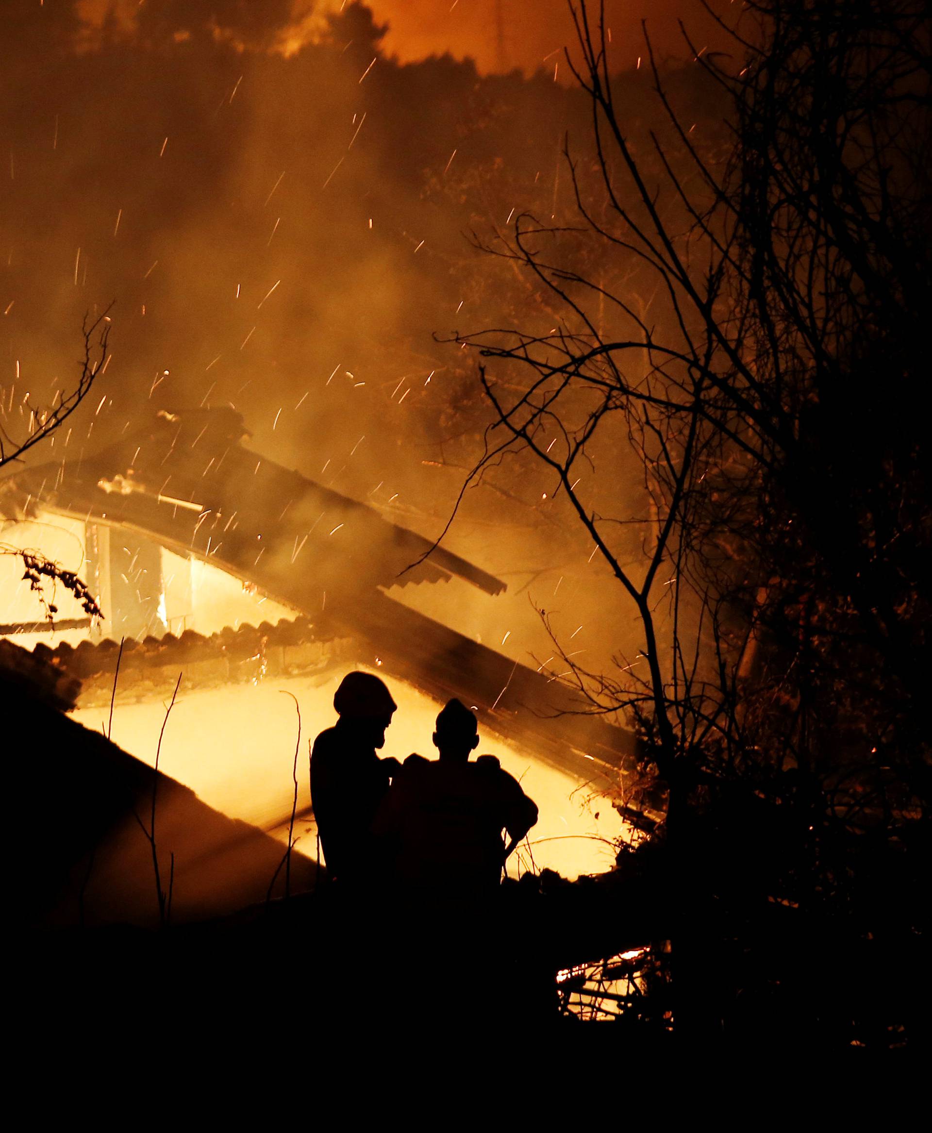 Firefighters try to extinguish a fire in a house as a wildfire burns near the village of Kalamos