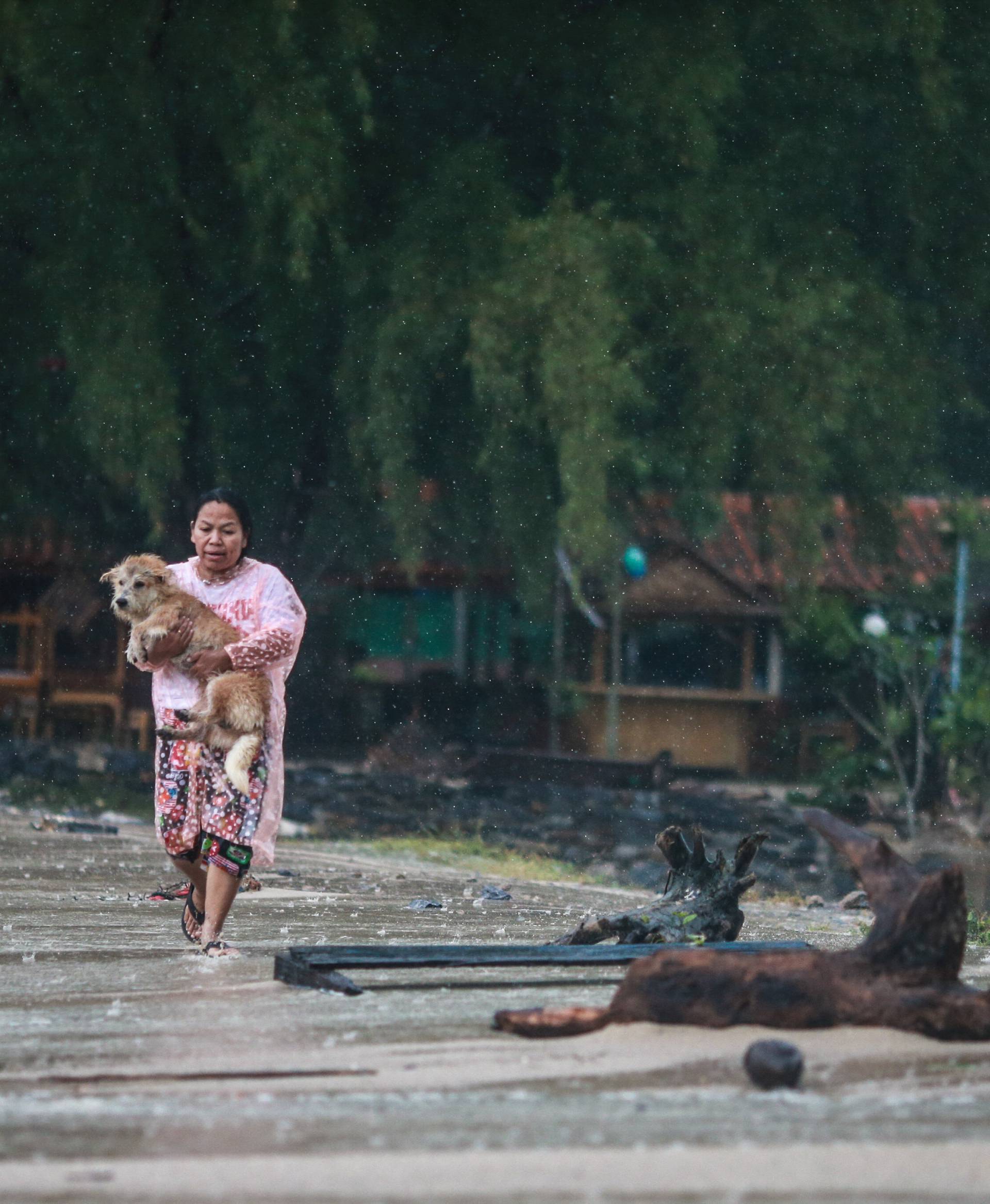 A woman holds up her dog as she runs toward her house as tropical storm Pabuk approaches the southern province of Nakhon Si Thammarat