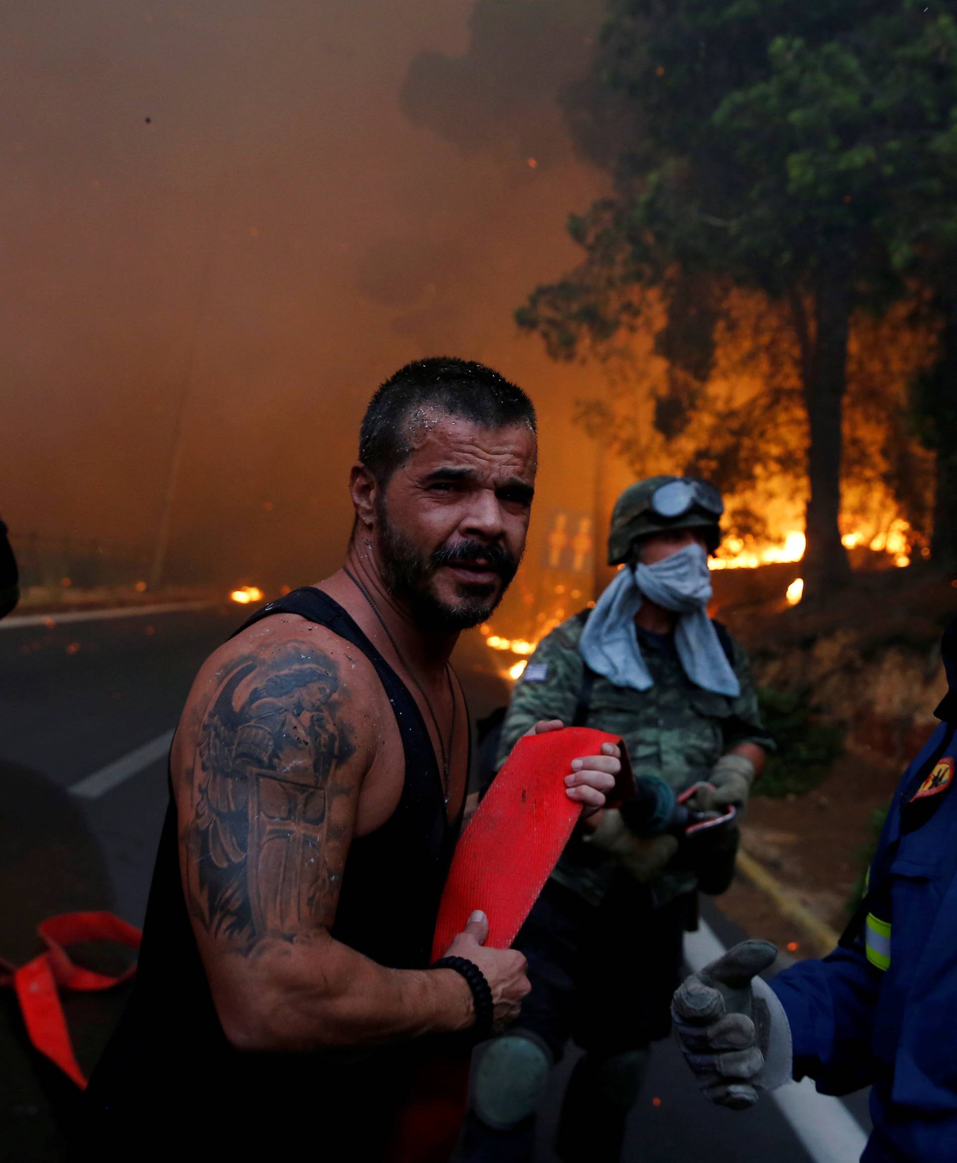 Firefighters, soldiers and local residents carry a hose as a wildfire burns in the town of Rafina, near Athens