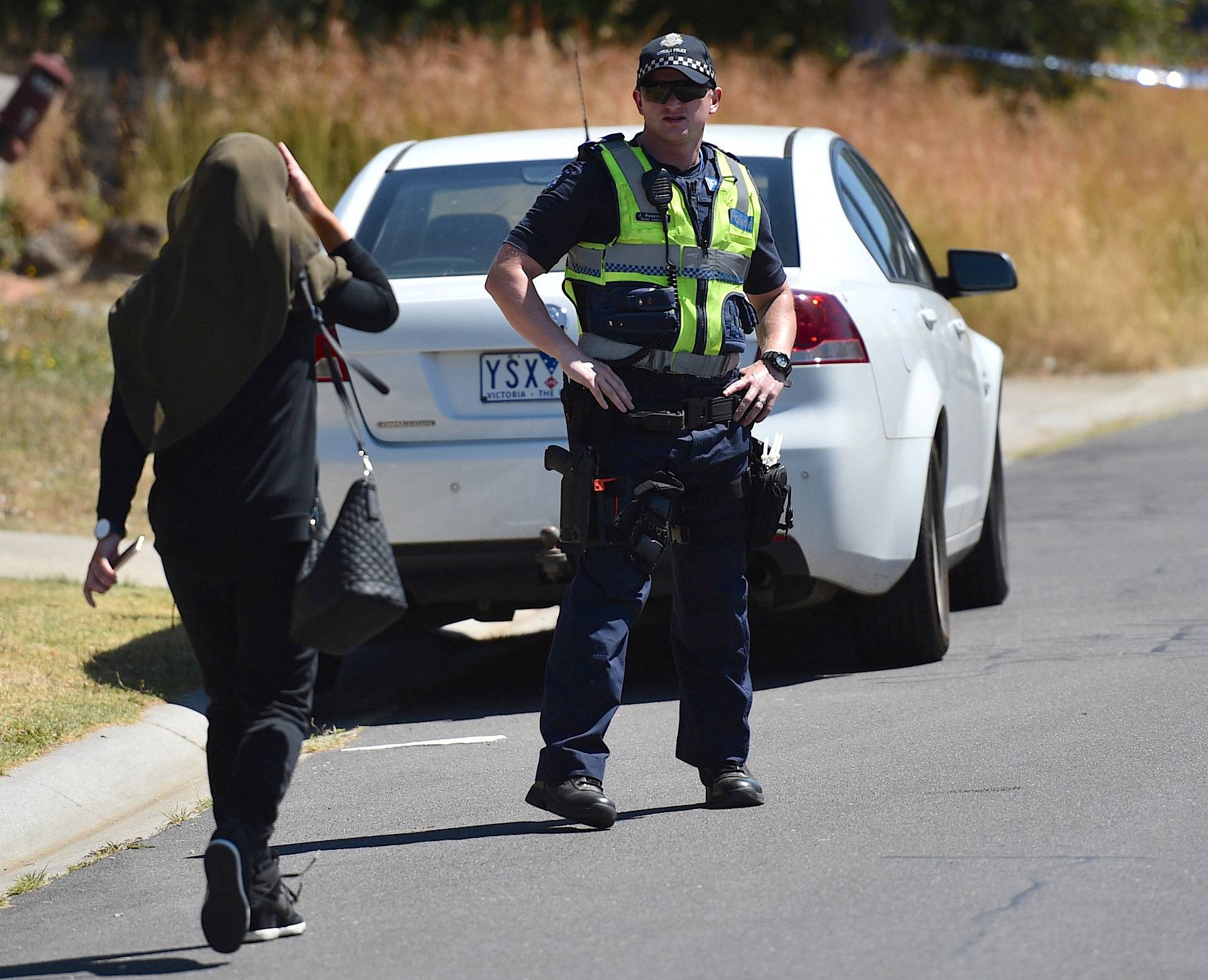 A woman approaches a policeman as he blocks the road during the search of a house in the Melbourne suburb of Meadow Heights, Australia