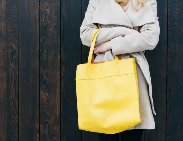 Fashionable beautiful big yellow handbag on the arm of the girl in a fashionable coat, posing near the wall. Part of body. Warm color.