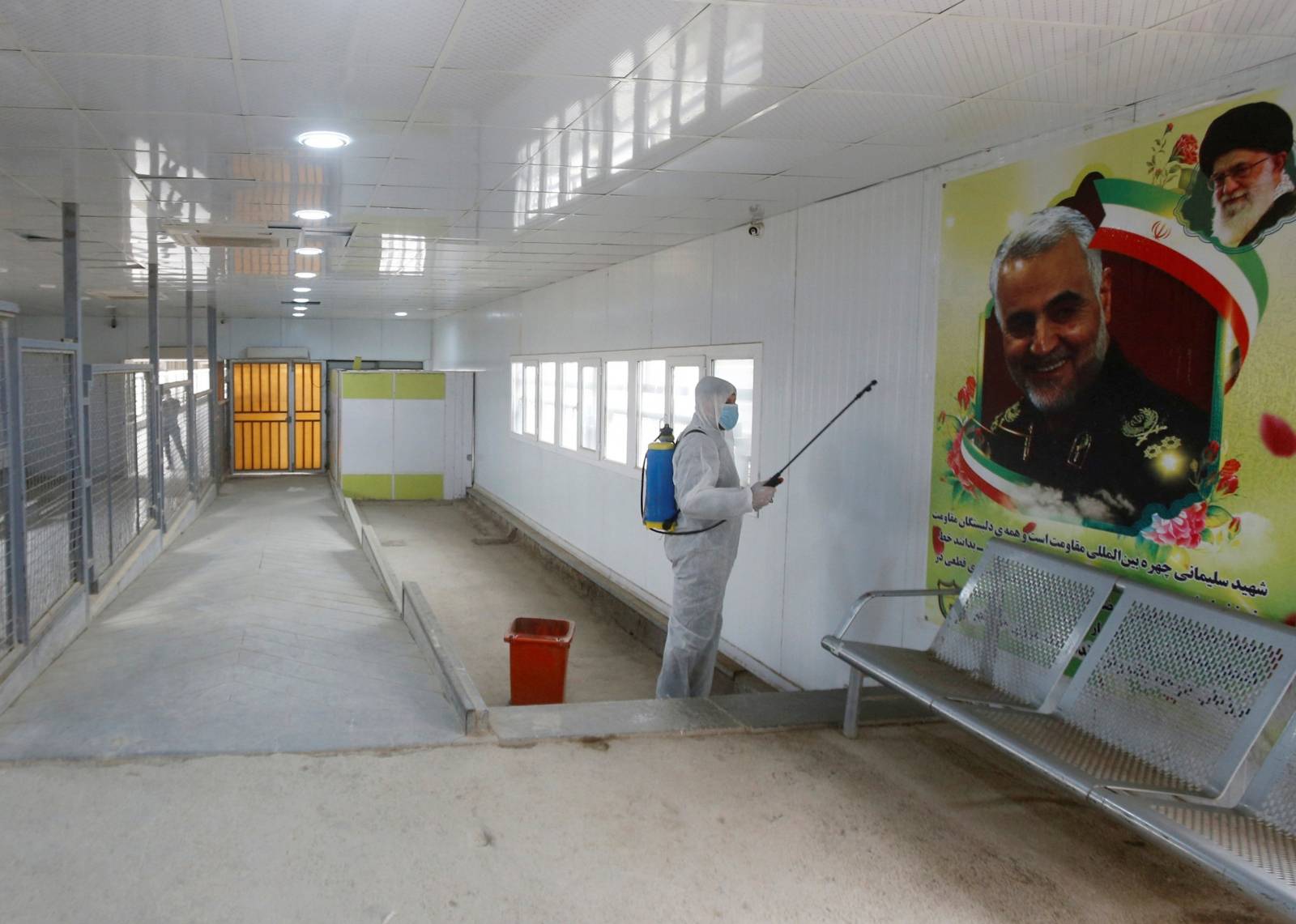 A worker in a protective suit sprays a disinfectant inside the gate of Shalamcha Border Crossing, after Iraq shut a border crossing to travellers between Iraq and Iran