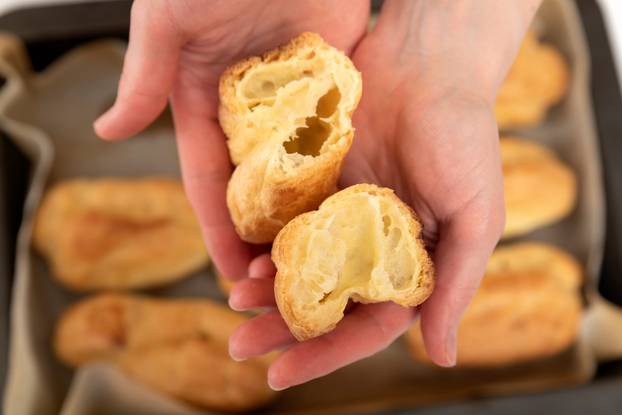 Middle of workpiece for profiteroles in hands of Chef. Puffs, popovers, eclair. Close up