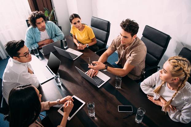 high angle view of multicultural business partners having meeting at table with laptops in modern office 