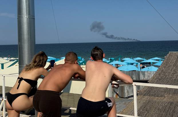 People look at a ship burning at sea in Odesa