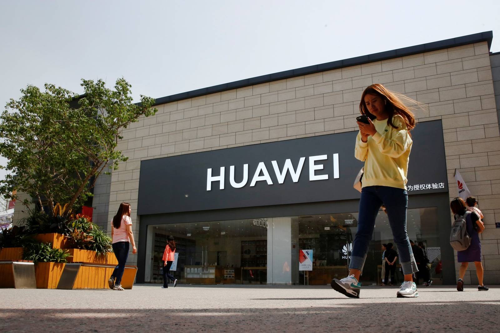 FILE PHOTO: A woman looks at her phone as she walks past a Huawei shop in Beijing